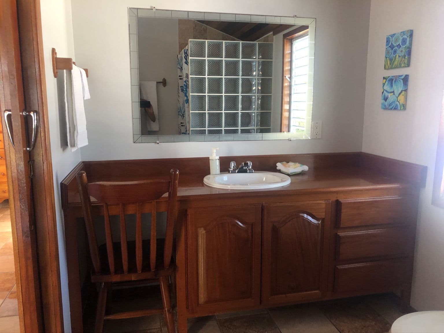 Bathroom vanity with sink and chair, mirror reflecting shower area