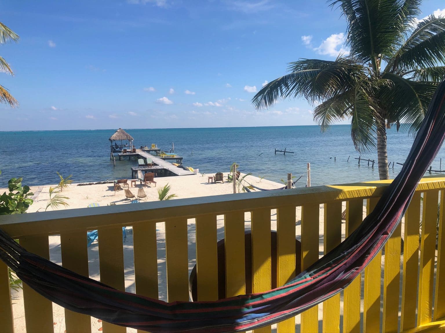 View from the balcony with hammock of the beautiful blue ocean, sandy beach, and waving palm trees