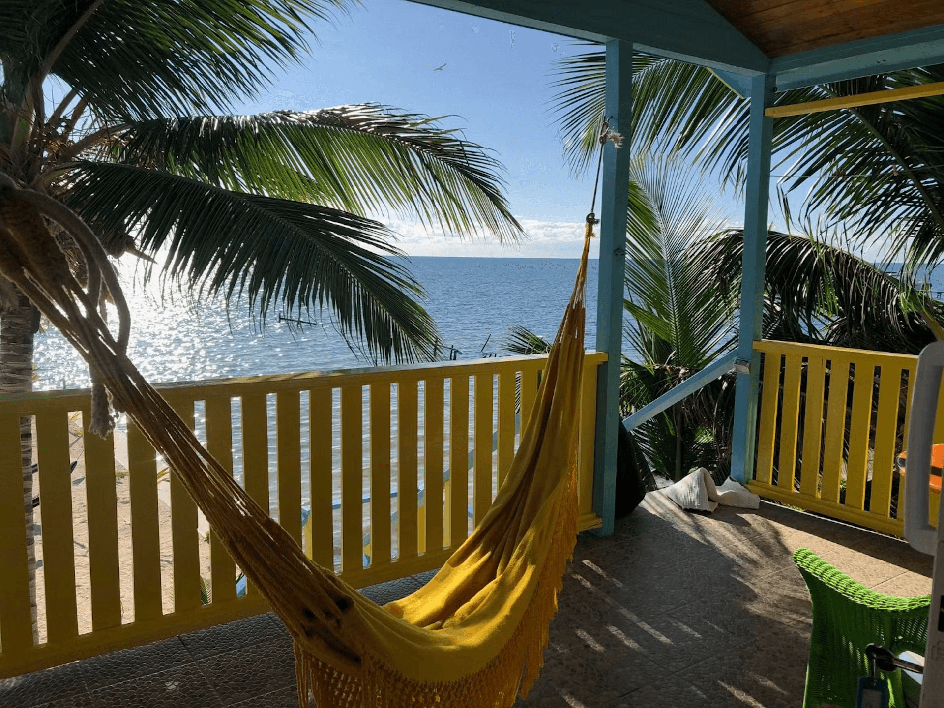 Brightly blue and yellow painted balcony with hammock and views of the ocean and palm trees