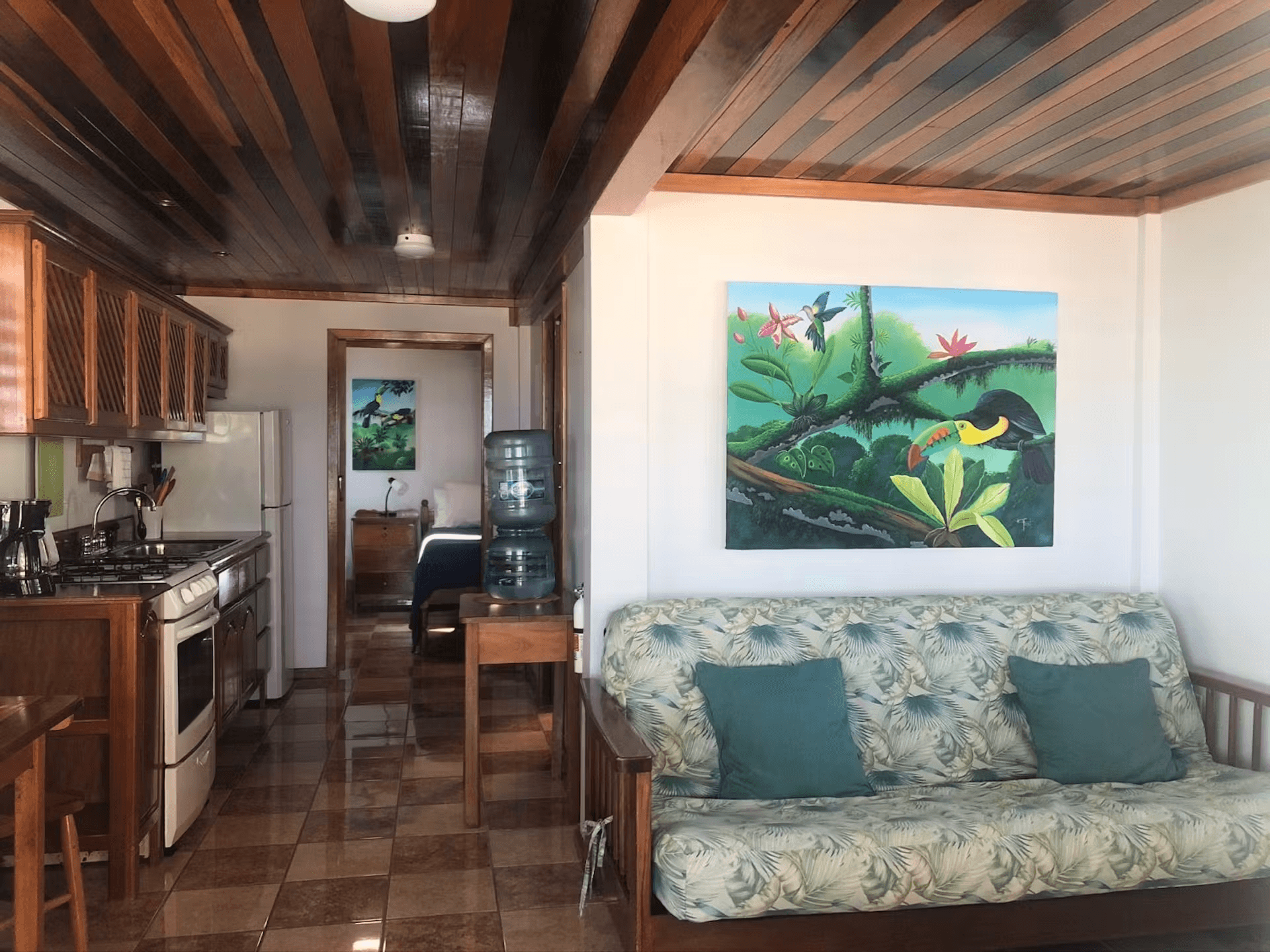 Sitting area with double futon, tropical artwork, hardwood ceilings, and kitchen to the left