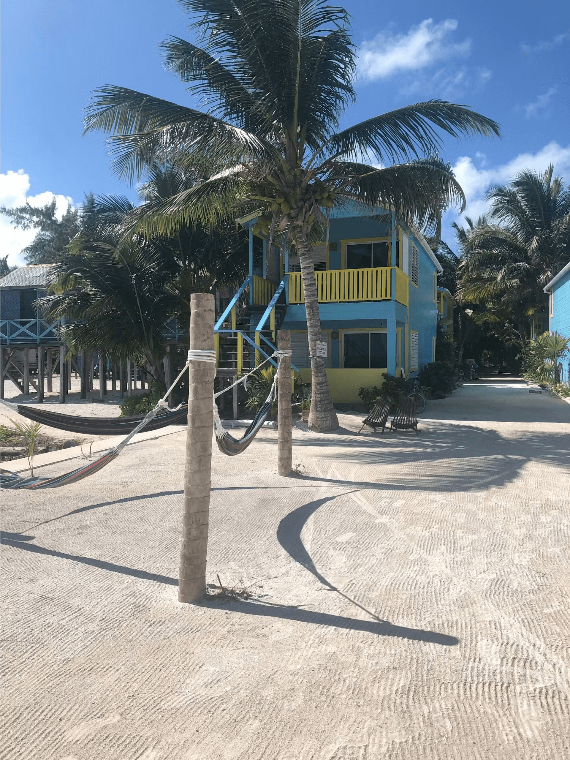 Sandy beach leading to brightly colored cabana surrounded by palm trees