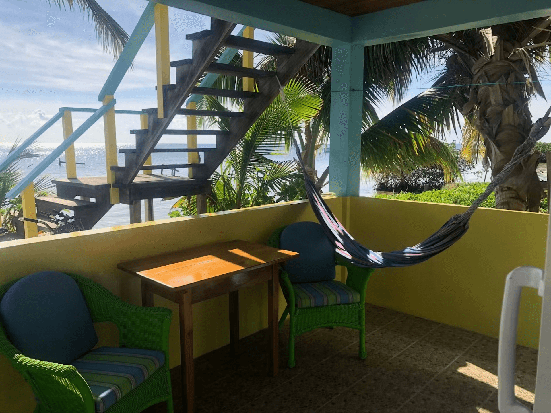 Brightly painted blue and yellow porch with hammock and wicker chairs with beach views