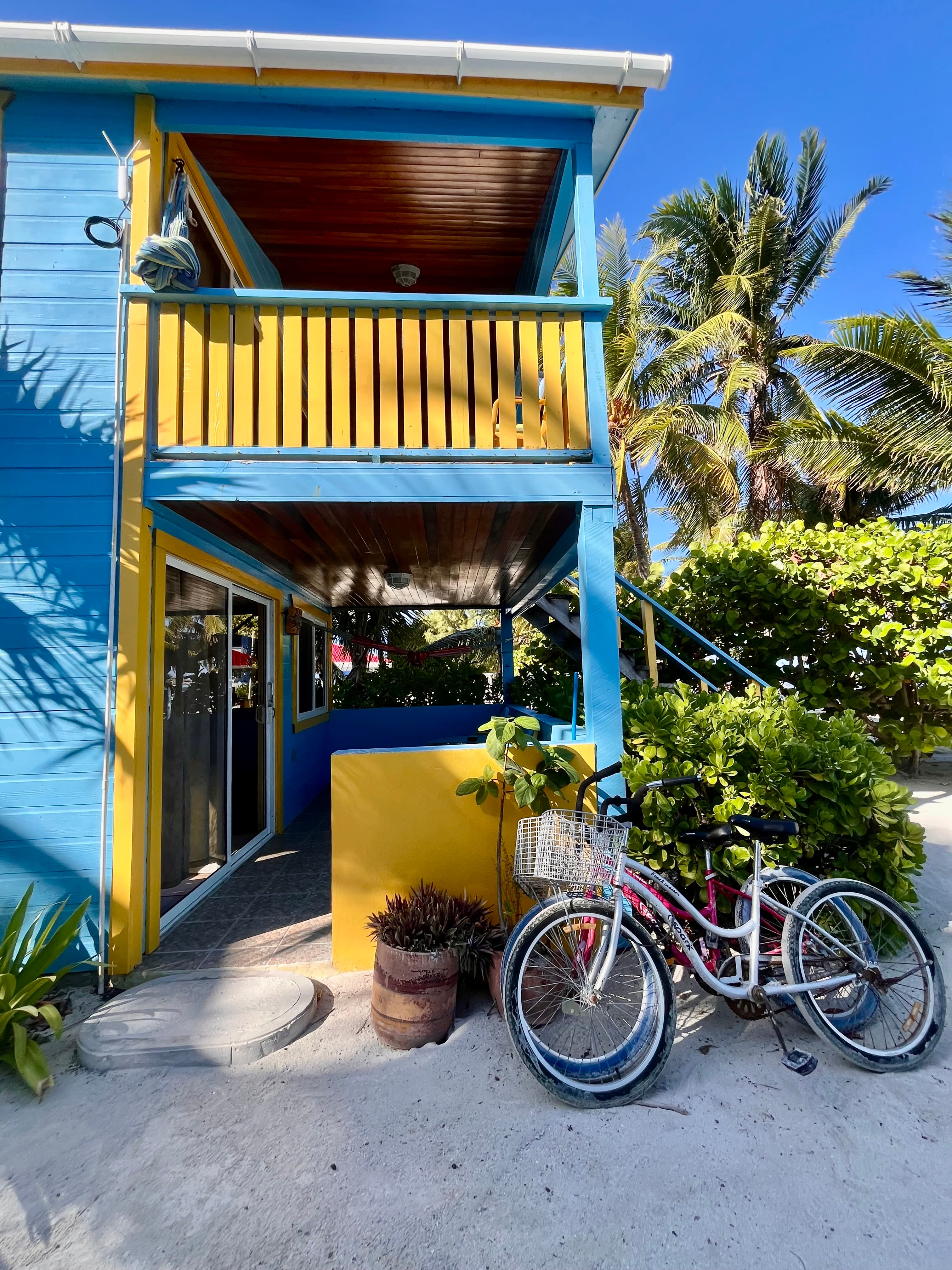 A brightly colored blue and yellow beach house with bicycles parked nearby, surrounded by tropical greenery.