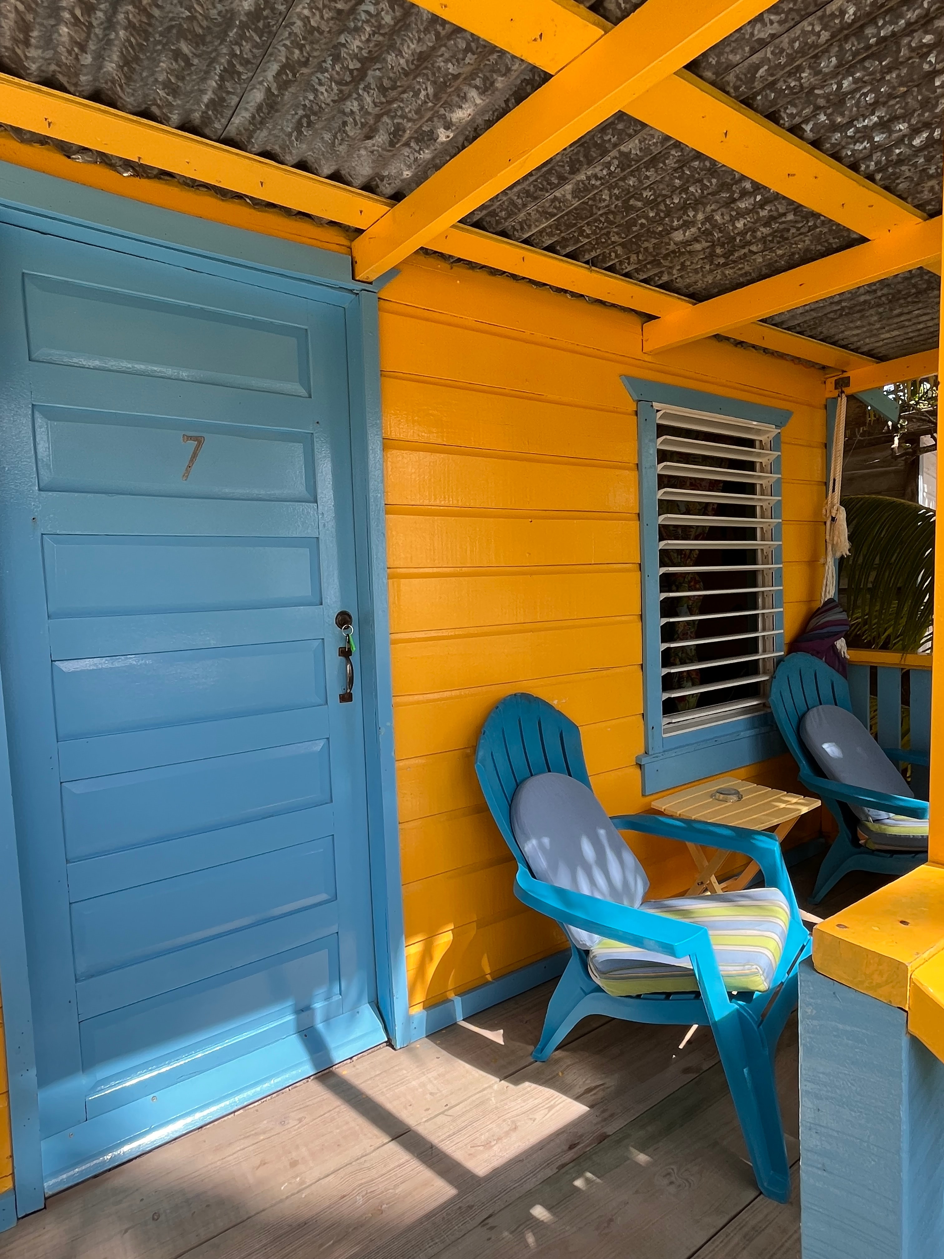 Vibrant yellow cottage exterior with a blue door and matching chairs on a porch.