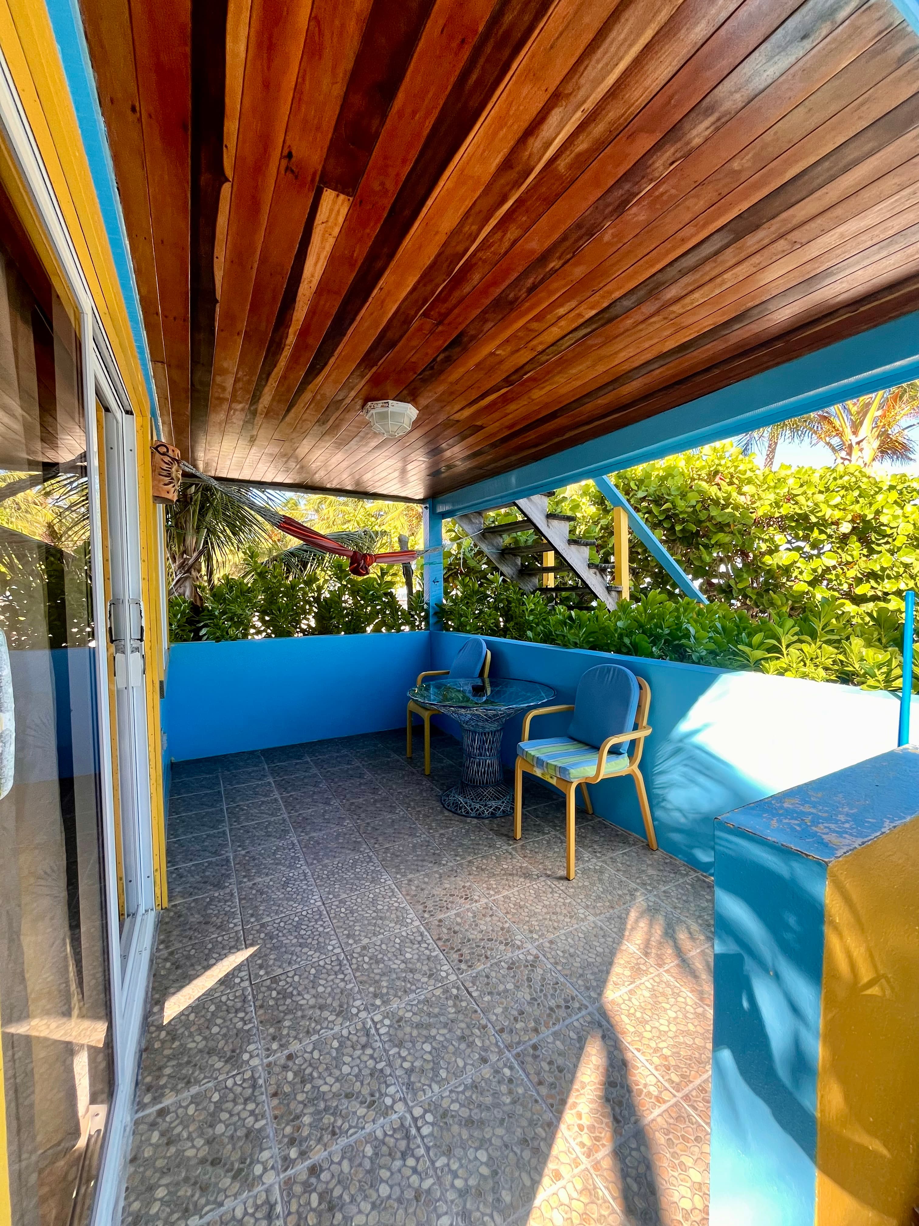 A cozy outdoor patio with blue walls, wooden ceiling, and two chairs beside a small table.