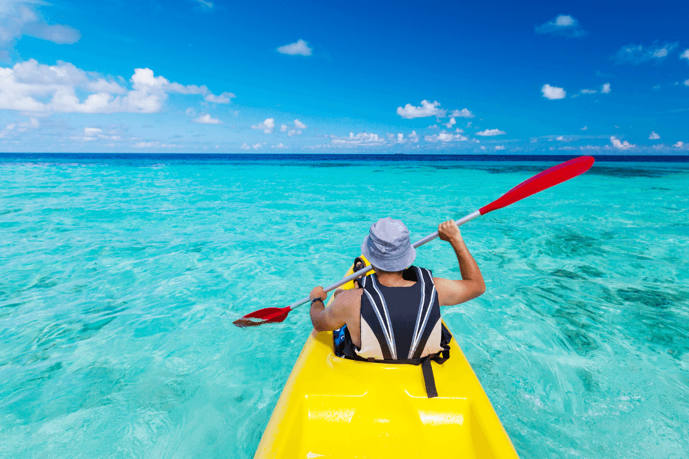 man in yellow kayak with hat and red paddle in blue ocean water
