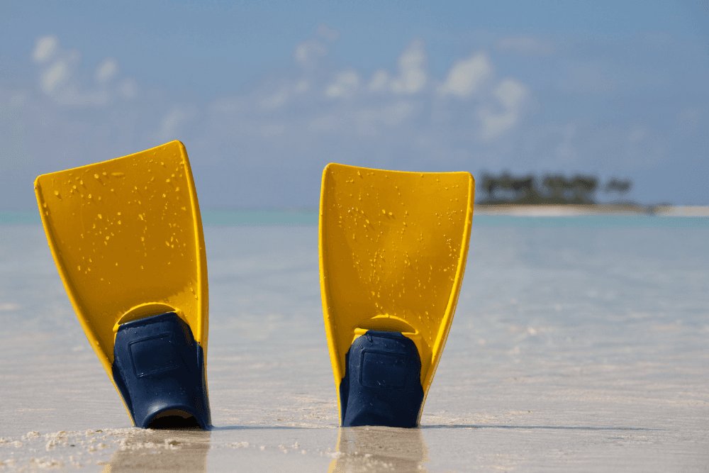 set of yellow flippers stuck in the sand with flipper part up with ocean in background